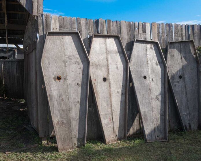 4,Coffin,Lids,Leaning,Against,A,Wooden,Fence