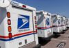 Row of USPS mail trucks parked in lot.