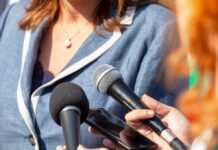 Person surrounded by microphones during an interview