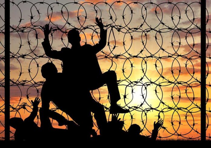 Silhouette of people helping each other over fence