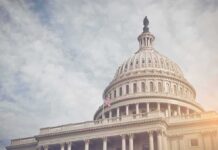 Capitol dome with American flag, under cloudy sky.