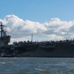Aircraft carrier on water under a cloudy sky.