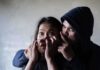 Man holding woman's mouth, gesturing silence.