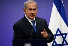 Man speaking at podium with Israeli flag behind him