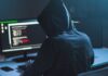 Person in hoodie using computer with code on screen.