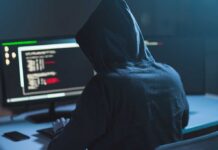 Person in hoodie using computer with code on screen.