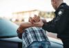 Police officer detaining person against car