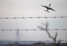 Airplane ascending above barbed wire fence sky background