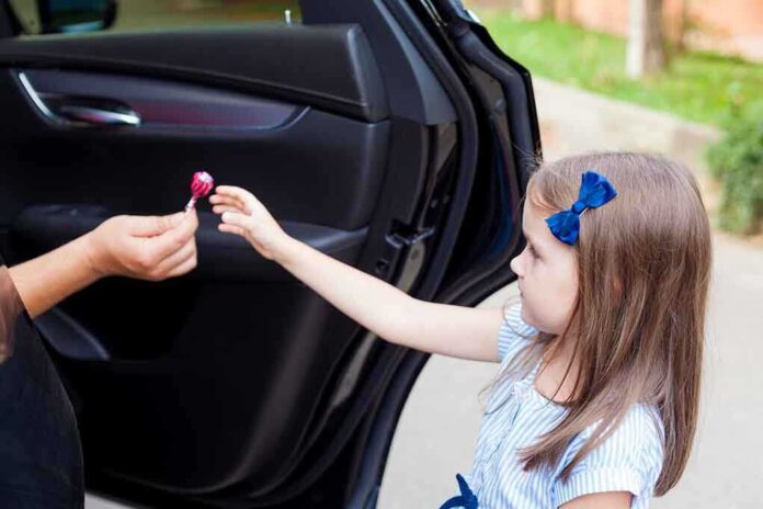 Child receiving lollipop from person in open car