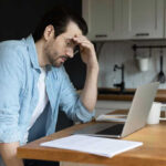 Man stressing over work on laptop at kitchen table
