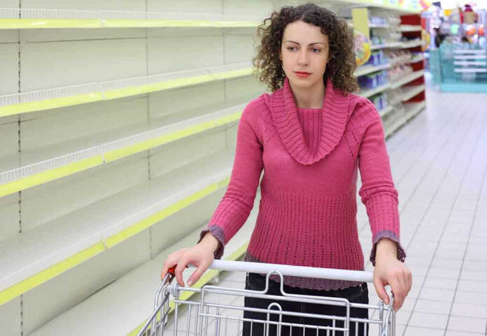 Woman with cart in store with empty shelves.