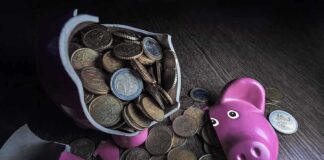 A broken pink piggy bank with coins spilling out onto a wooden surface