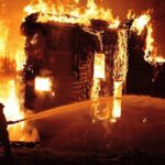 Texas Inferno: Masked Attacker Still Loose A firefighter battling a large house fire at night