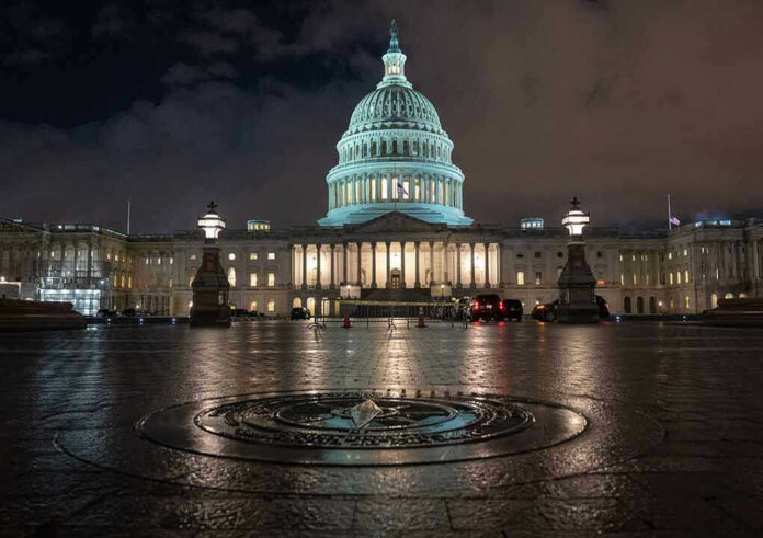 U.S. Capitol building illuminated at night with wet pavement.