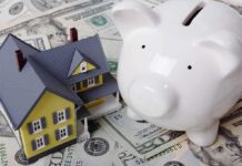 A model house next to a white piggy bank on a bed of dollar bills