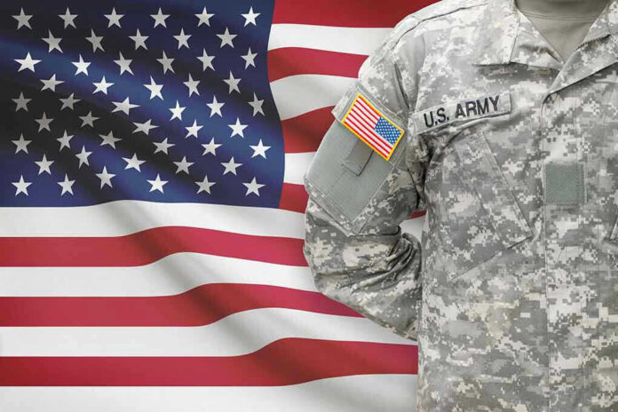 247938520 Soldier in camouflage uniform standing before American flag