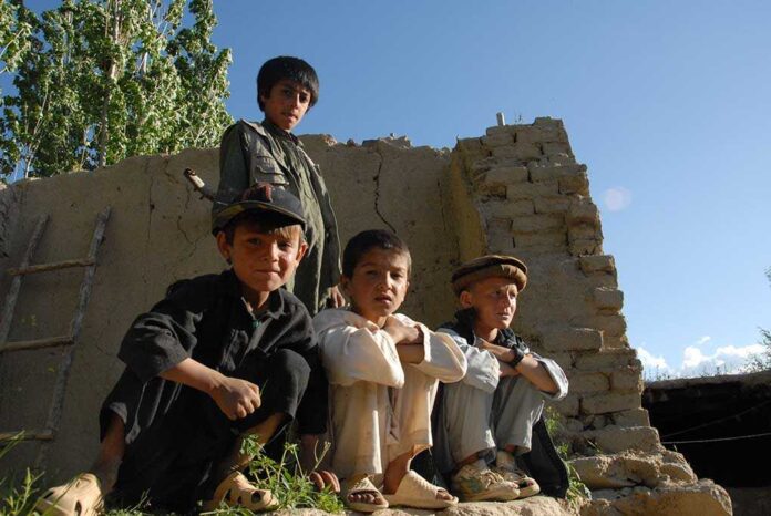 Four boys sitting and standing near a crumbling wall in a rural area