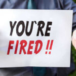Person holding YOURE FIRED sign.