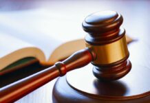 A wooden gavel resting on a round base with an open law book in the background
