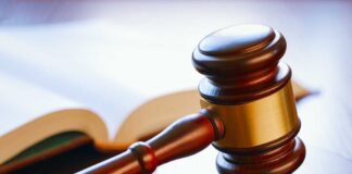 A wooden gavel resting on a round base with an open law book in the background