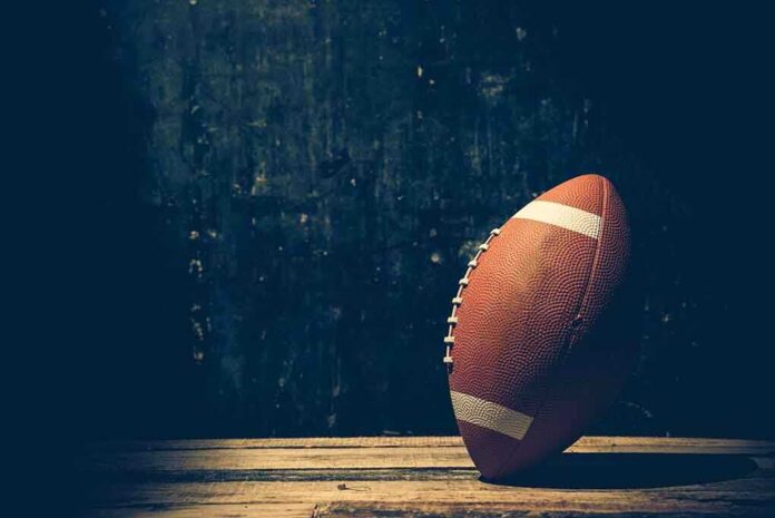 An American football resting on a wooden surface against a dark background