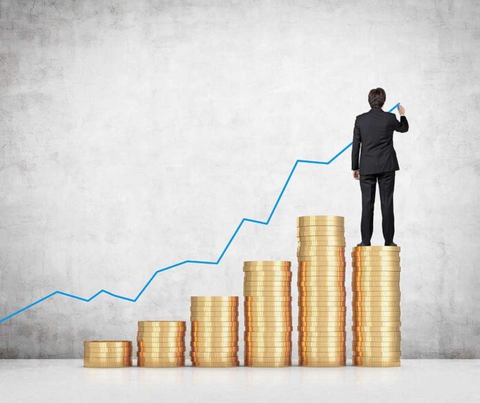Businessman standing on stacks of coins, drawing a growth chart