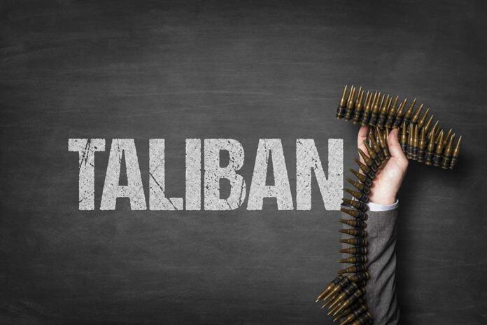shutterstock_1327780076 (1).jpg A hand holding a belt of ammunition in front of the word TALIBAN on a dark background