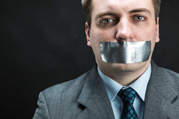 Man in business attire with duct tape over his mouth, conveying a message about silence