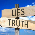 Signs pointing to Lies and Truth against sky.