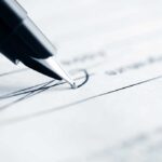 Close-up of a pen poised above a document with handwritten lines