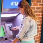 Massive ATM Fraud Ring BUSTED – 87 Arrested Young woman using an ATM in an urban environment