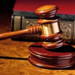 A wooden gavel resting on a polished surface with a law book in the background