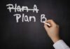 A hand writing Plan B on a chalkboard with Plan A crossed out