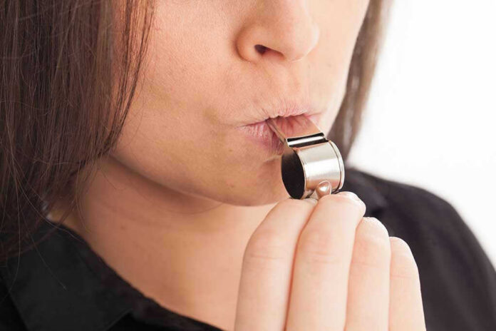 1455310238 Person blowing a silver whistle close-up.