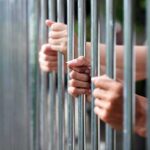 Hands gripping metal prison bars