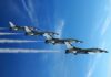 Four military jets flying in formation against a blue sky, leaving smoke trails