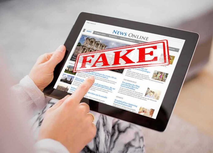 Person holding a tablet displaying a news website with a 'FAKE' stamp
