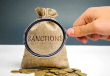 Hand holding magnifying glass over sack labeled Sanctions.