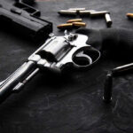 MASSIVE Shootout–Gunman’s Chilling Past Revolvers and bullets on a dark surface.