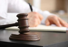 Judges gavel on desk with person writing.
