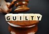 A gavel striking down next to wooden blocks spelling 'GUILTY'