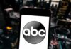 A smartphone displaying the ABC logo against a blurred urban background