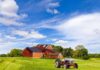 A vintage tractor in front of a red barn on a sunny day