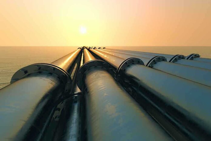 Industrial pipes extending towards the horizon over water during sunset