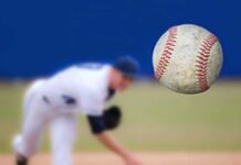 A baseball in mid-air with a pitcher in the background preparing to throw