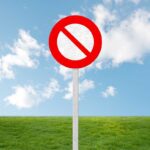 A no entry sign on a grassy field under a clear blue sky