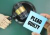 A wooden gavel next to a hand holding a blue card that says 'PLEAD GUILTY'