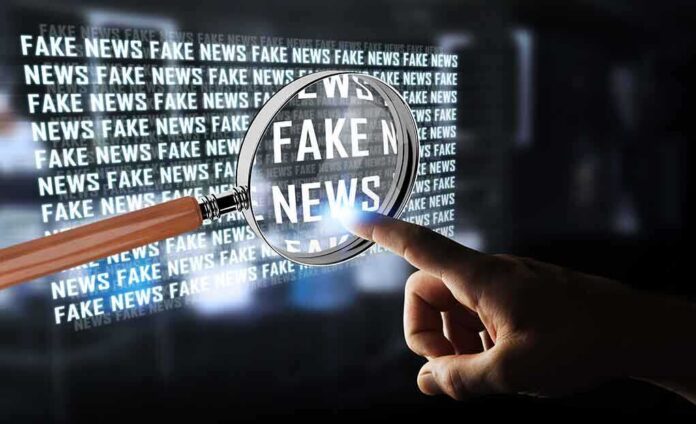A hand pointing at the words 'FAKE NEWS' magnified by a glass