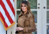 Woman in brown coat beside American flag.