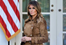 Woman in brown coat beside American flag.